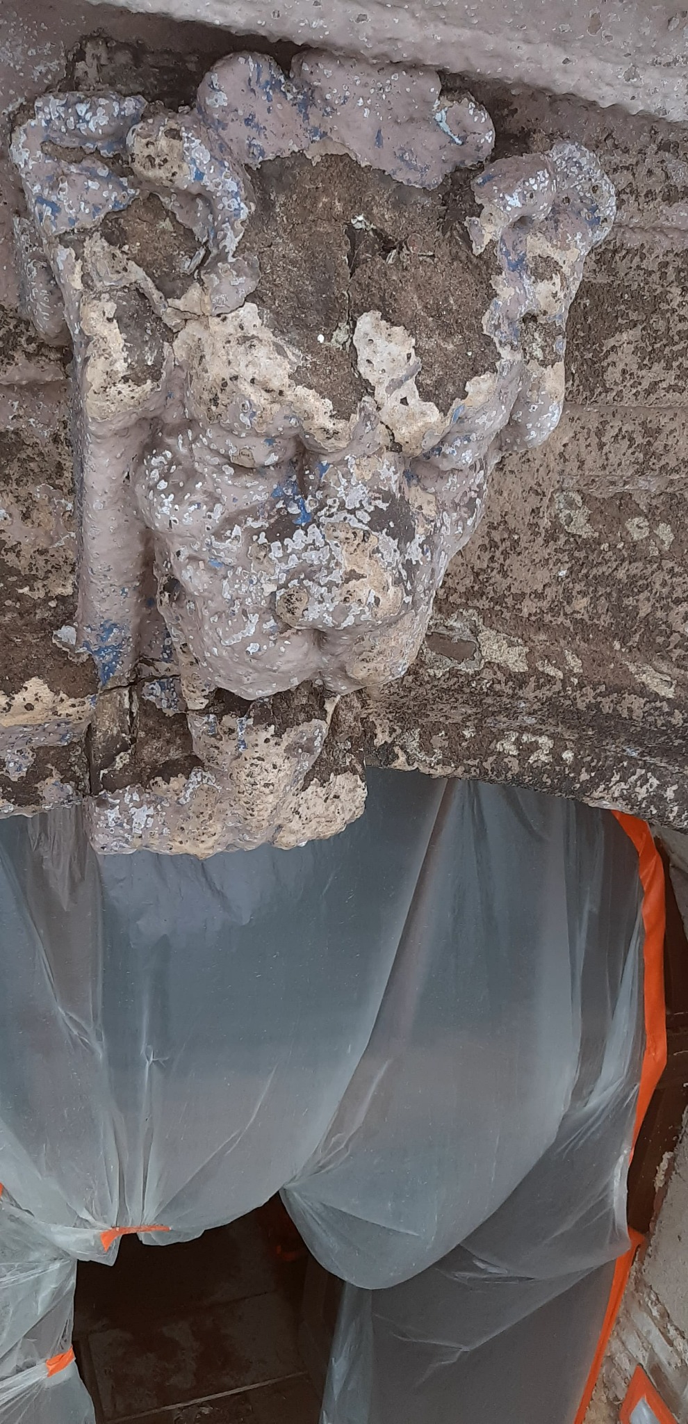 Fragment elewacji z dekoracyjnym elementem architektonicznym, w trakcie przygotowań do prac renowacyjnych, zabezpieczony folią ochronną.