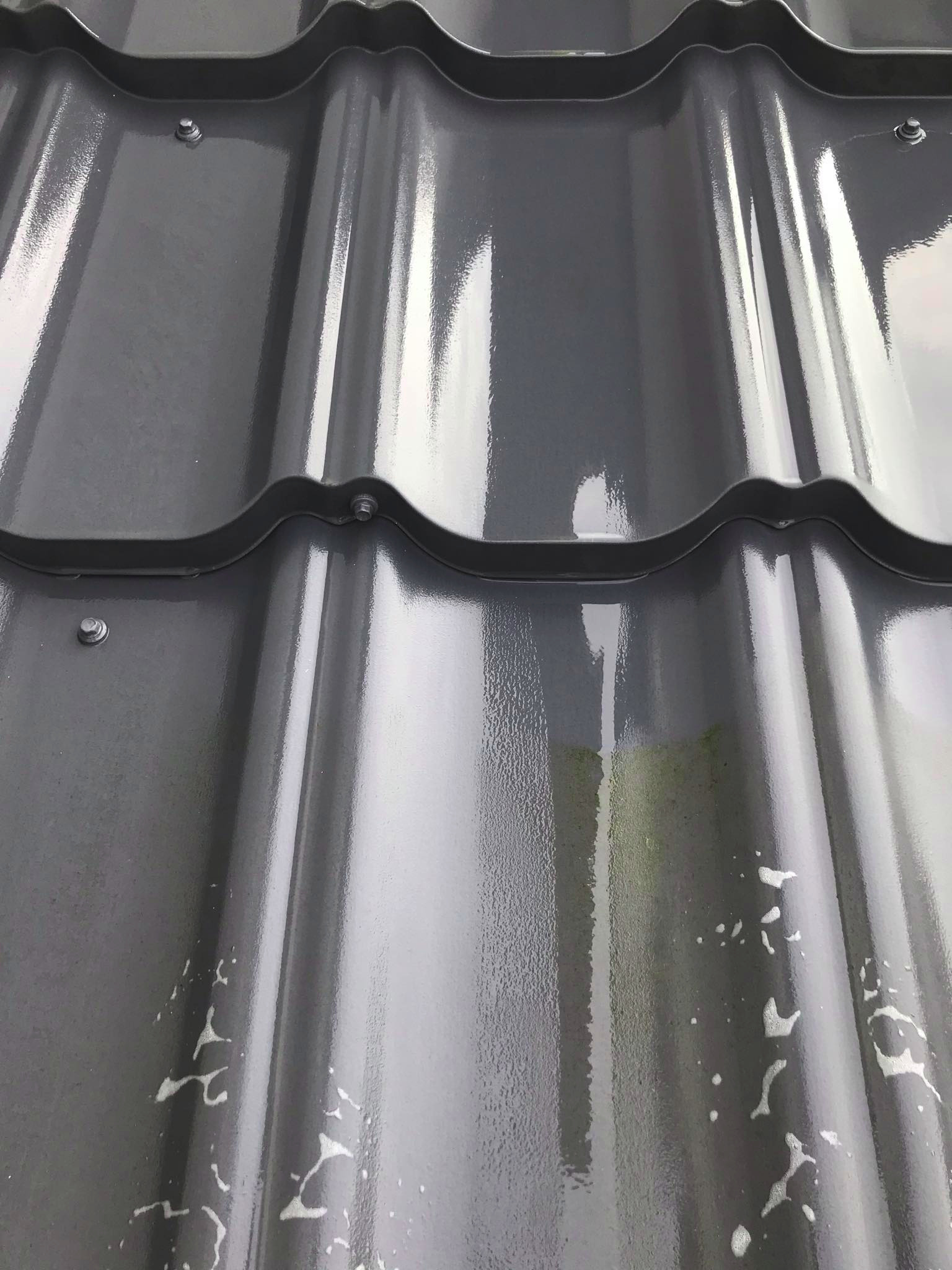 Błyszczące, szare panele dachowe z widocznymi śladami po niedokładnym czyszczeniu, krople wody lub resztki detergentu na powierzchni.
