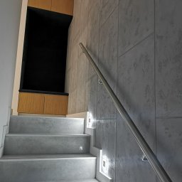 LukArt Łukasz Linczowski - Schody z szarymi stopniami, podświetleniem LED w ścianie i metalową poręczą, obok wnęka z drewnianymi szafkami.