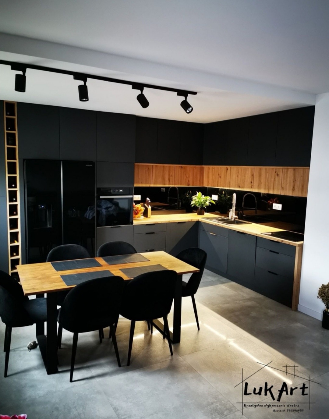 Nowoczesna kuchnia w Rzeszowie z czarnymi matowymi szafkami, drewnianym blatem i stołem z czarnymi krzesłami. Oświetlenie podszafkowe podkreśla naturalne drewno.
