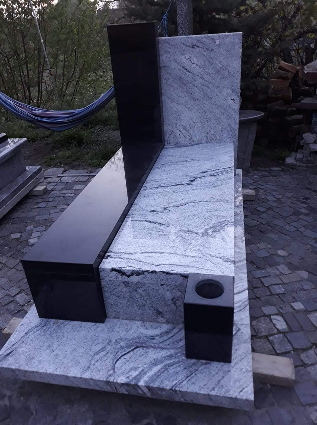 Nowoczesny nagrobek z jasnego granitu z ciemnymi elementami, widoczny hamak w tle.