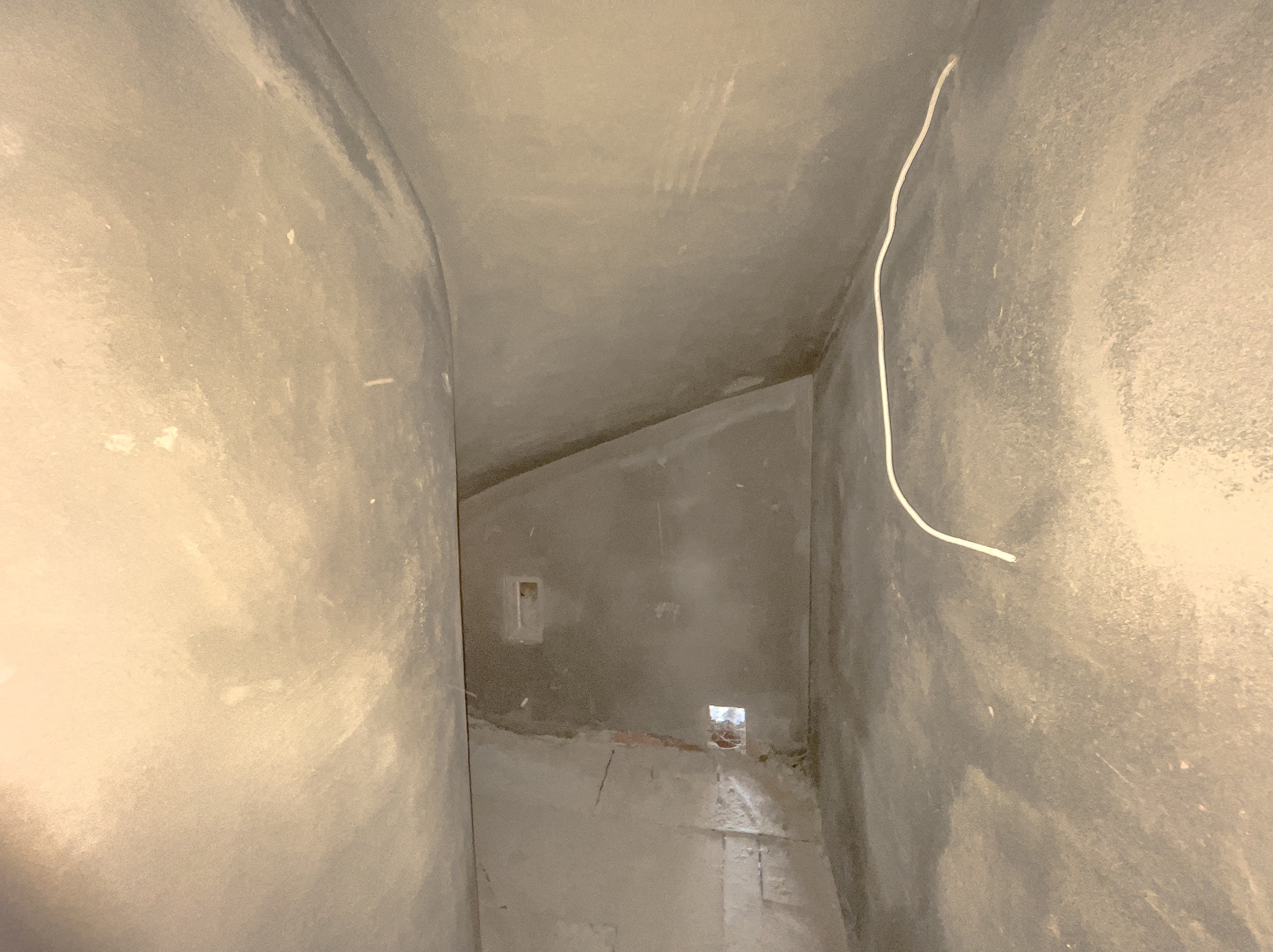 Wnętrze pomieszczenia po nałożeniu szarego tynku maszynowego, widoczne wystające przewody elektryczne i otwory na puszki pod gniazdka.