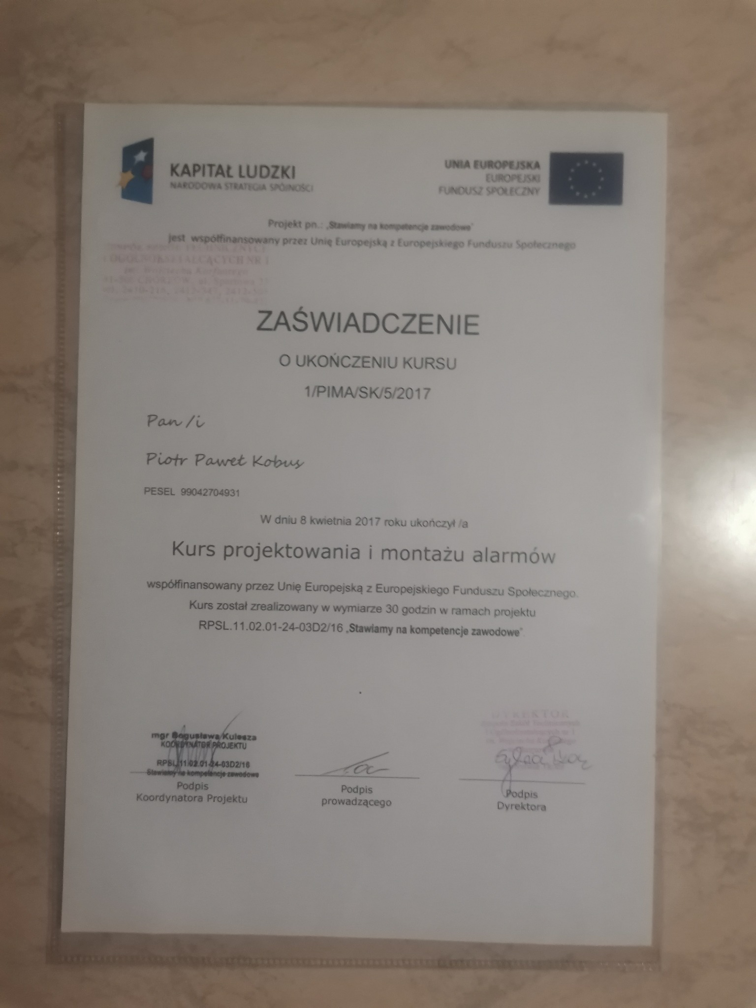 Skan zaświadczenia o ukończeniu kursu projektowania i montażu alarmów, wydanego w 2017 roku, z widocznymi podpisami koordynatora projektu i dyrektora.