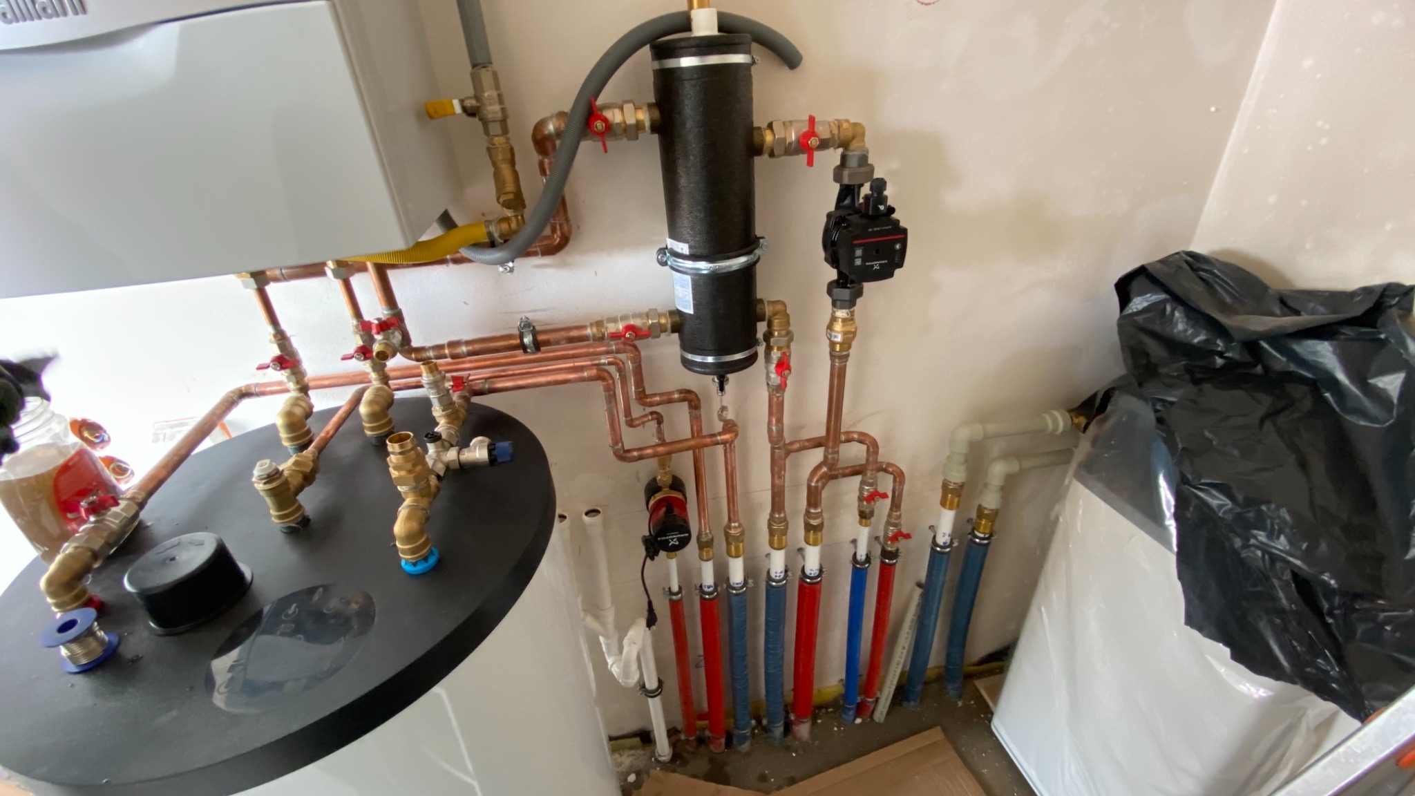 Nowa instalacja centralnego ogrzewania z miedzianymi rurami, pompą obiegową i zbiornikiem wyrównawczym, widoczne lutowanie i materiały instalacyjne.