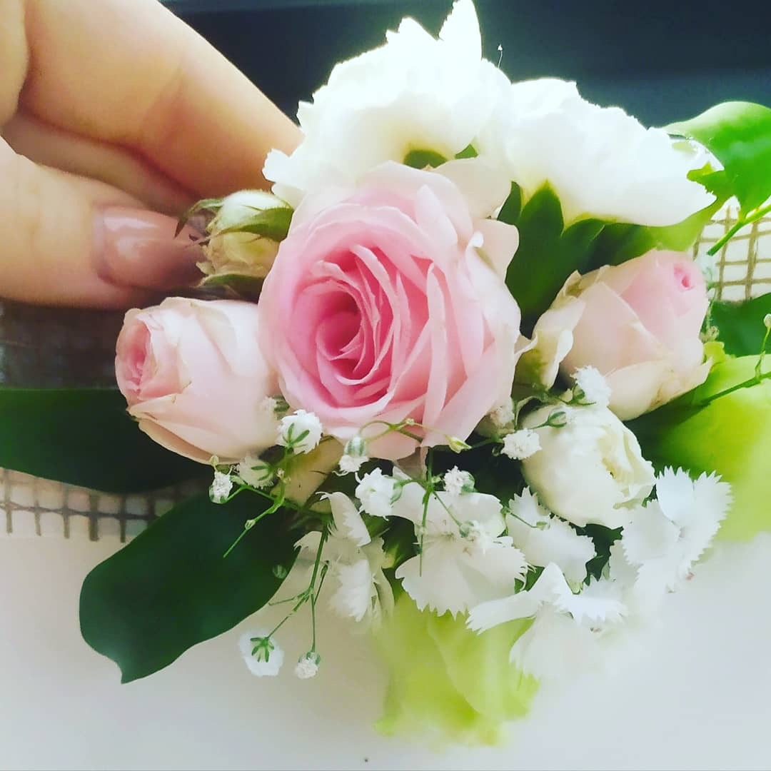 Delikatny bukiecik z różowych róż i białych goździków, trzymany w dłoni z jasnym manicure, na jasnym tle.