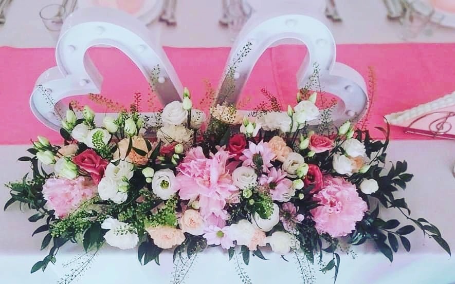 Dekoracja stołu weselnego: bukiet z różowych i białych kwiatów, podświetlane serca w tle, różowy bieżnik.