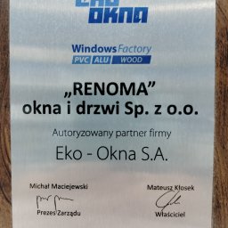 Renoma Okna i Drzwi - Metalowa tabliczka informacyjna firmy Renoma, autoryzowanego partnera Eko-Okna S.A., z logo Eko-Okna, adresem firmy i podpisami Prezesa Zarządu i Właściciela, umieszczona na drewnianym tle.