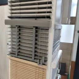 Ekspozycja różnych typów żaluzji poziomych: drewniane, PCV i pionowe, z widocznymi mechanizmami sterującymi i różnymi kolorami lameli.