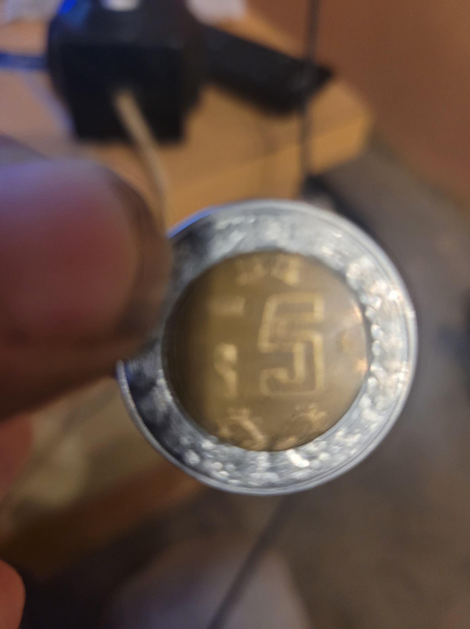 Moneta 5 zł w dłoni, ukazująca detale i fakturę. Niejasne tło. Słaba jakość zdjęcia.