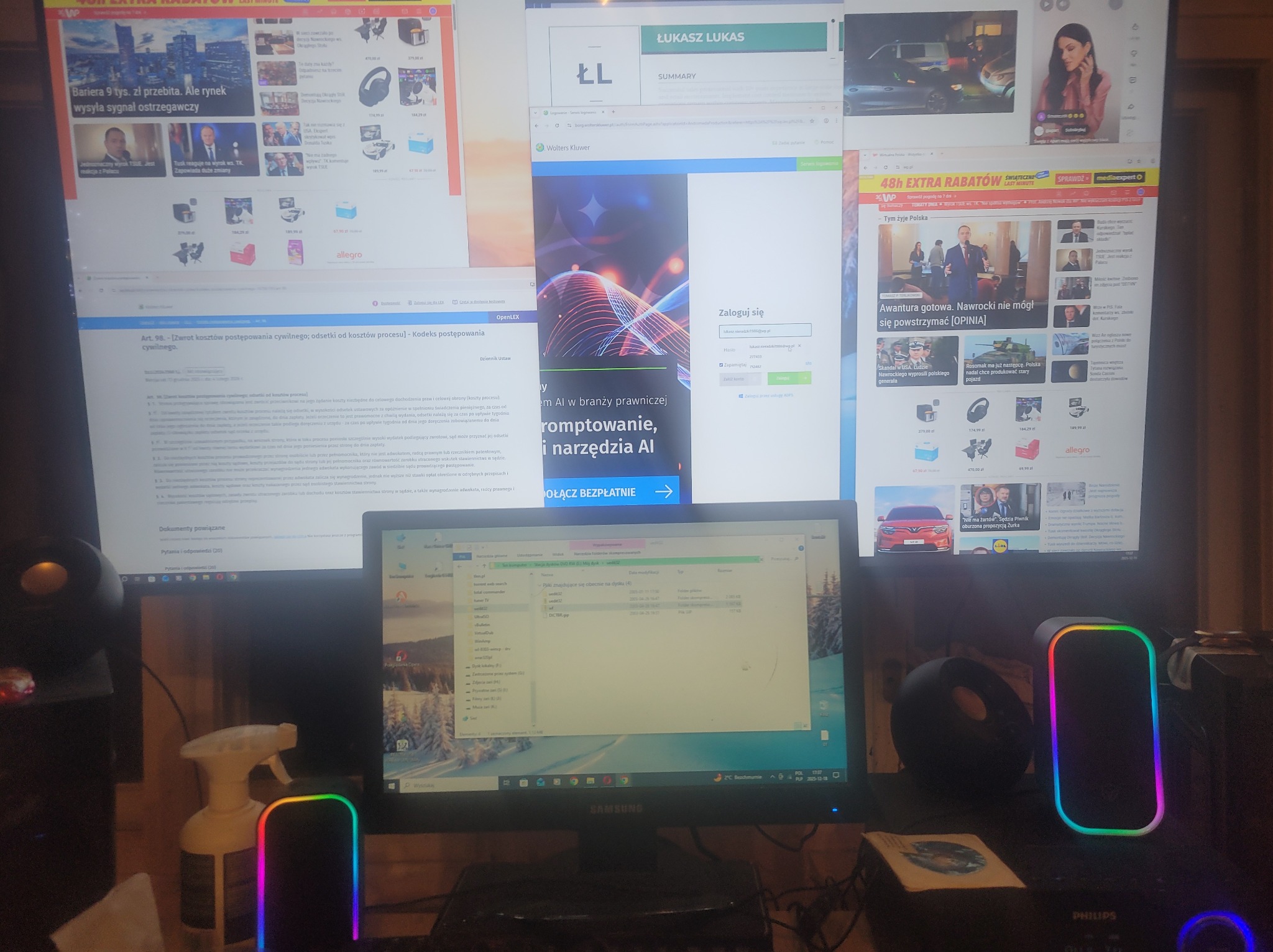 Rozbudowane stanowisko pracy z wieloma monitorami wyświetlającymi strony internetowe i okna programów, otoczone głośnikami z podświetleniem RGB.