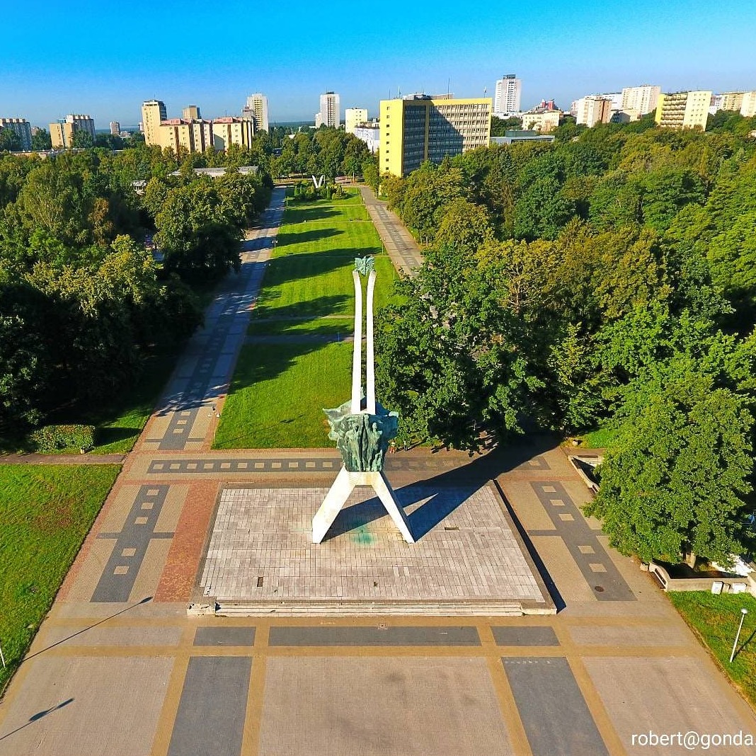 Panorama z lotu ptaka przedstawiająca pomnik Trzech Krzyży w Gdańsku, otoczony zielenią parkową i zabudową miejską w tle, sfotografowany w słoneczny dzień.