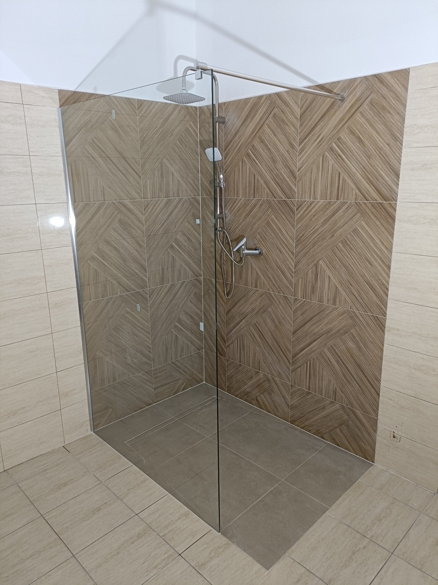 Nowoczesna kabina prysznicowa walk-in z deszczownicą i panelami ściennymi w geometryczny wzór, wykończona w beżach i brązach, z odpływem liniowym w podłodze.