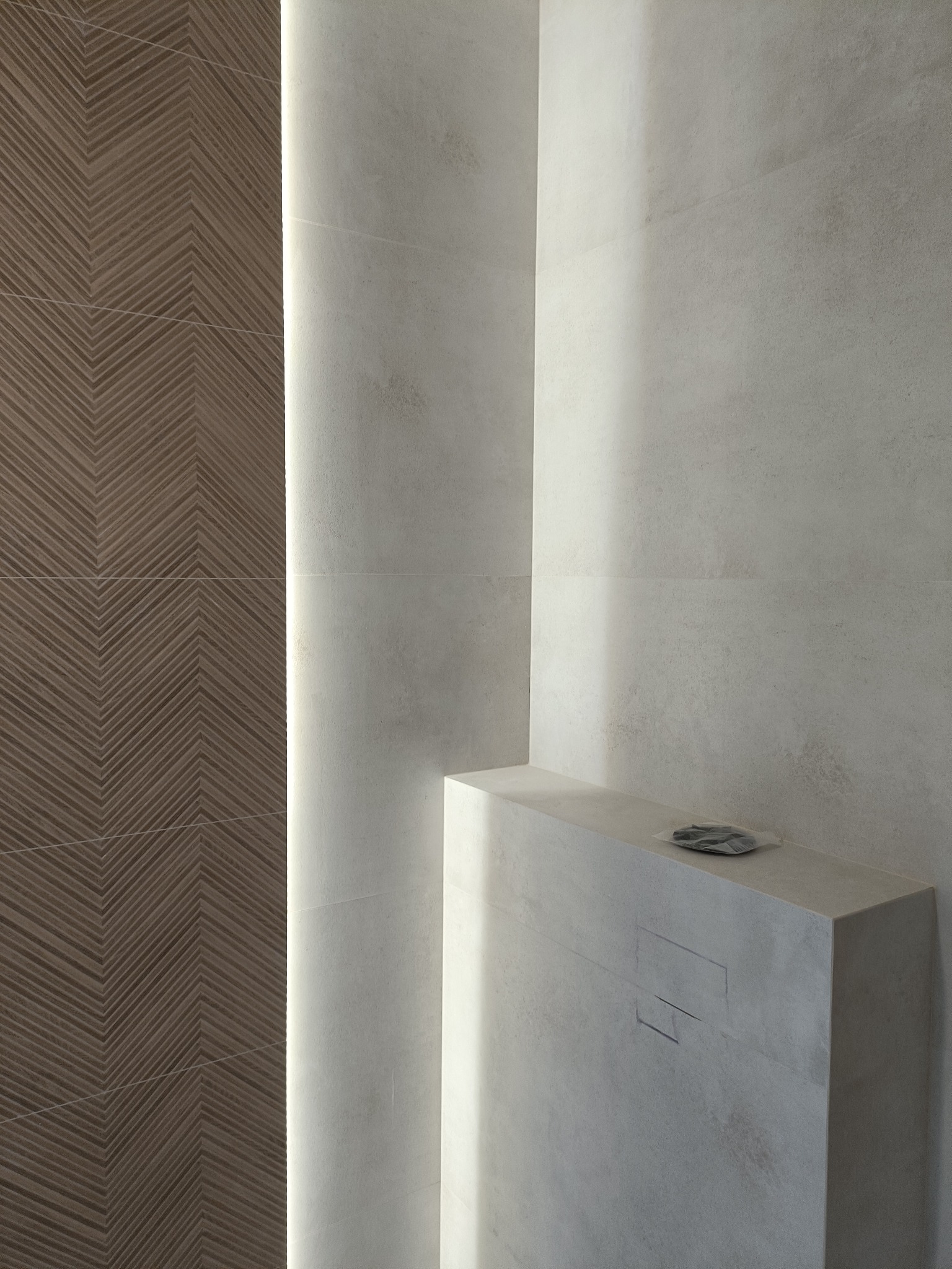 Minimalistyczna łazienka z akcentem drewnopodobnych płytek ułożonych w jodełkę, podświetlonych pionową listwą LED. Jasne, matowe płytki na pozostałych ścianach i zabudowie.