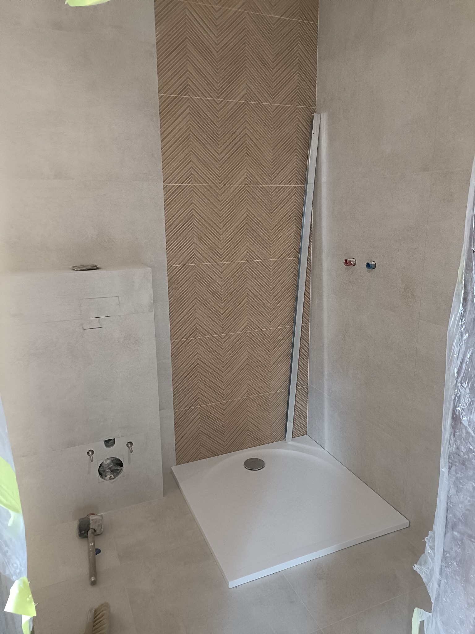 Montaż brodzika i płytek z wzorem jodełki w łazience w Nowej Dębie. Widoczne przyłącza wodne i stelaż podtynkowy WC. Etap prac wykończeniowych.