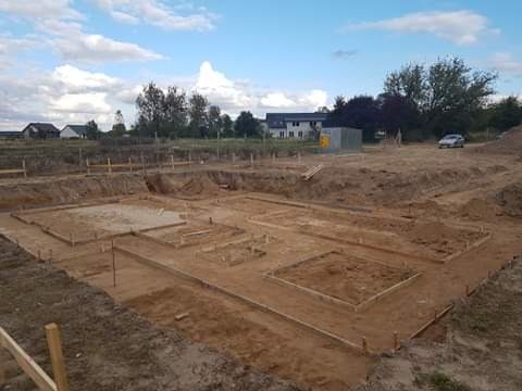Przygotowanie terenu pod fundamenty domu jednorodzinnego w Boleszkowicach, widoczne wykopy i szalunki pod wylewkę, w tle zabudowa mieszkalna i błękitne niebo.