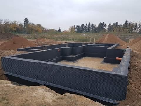 Fundamenty domu jednorodzinnego z izolacją przeciwwilgociową, widoczne wykopane podłoże i przygotowany teren pod budowę.