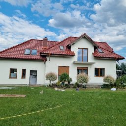 Kamil susel - Dom jednorodzinny we Wrocławiu z jasną elewacją i czerwoną dachówką, widok z trawnika. Na elewacji widoczne świeże ślady malowania.