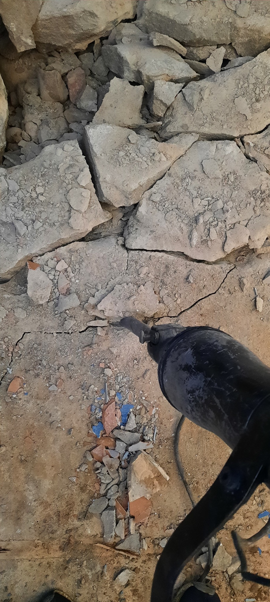 Praca z młotem udarowym przy rozbiórce ściany z gruzem ceramicznym w tle.