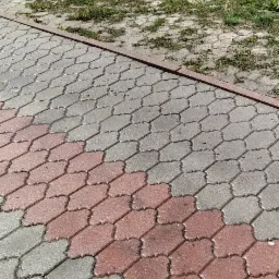 Częściowo umyta kostka brukowa w kolorze szarym i czerwonym z resztkami trawy i liści na powierzchni, widok z góry.