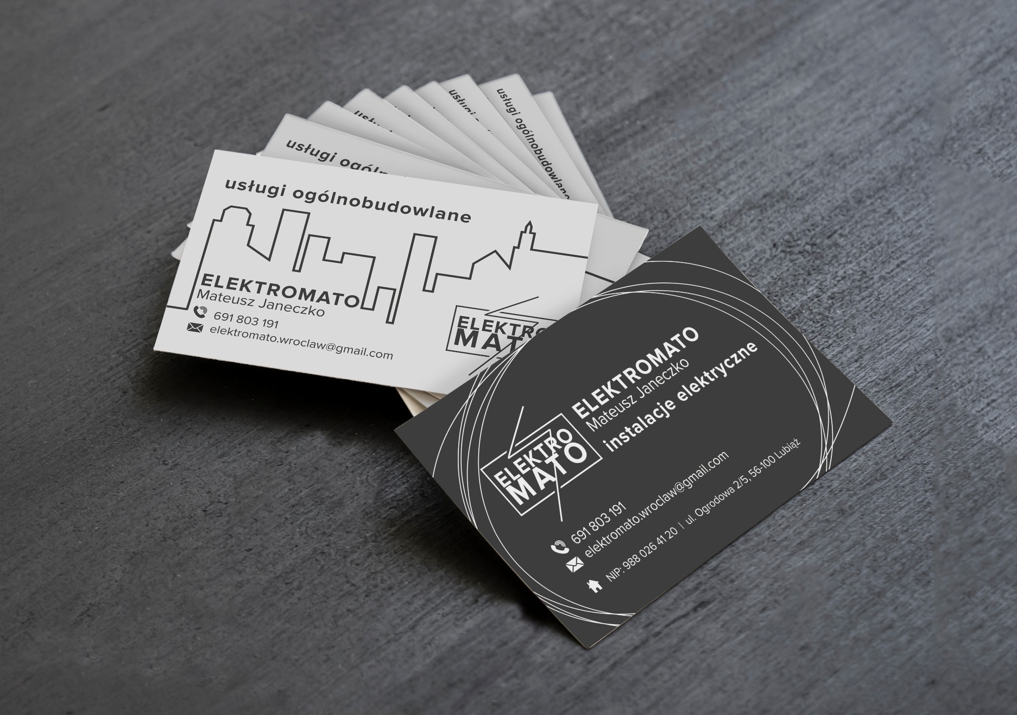 Wizytówki firmy Elektromato Mateusz Janeczko, oferującej usługi ogólnobudowlane i instalacje elektryczne, ułożone wachlarzowo na szarym tle.