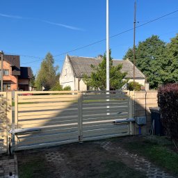 KLIMERA Michał Garbiec - Automatyczna brama przesuwna w kolorze beżowym, zamontowana przed domem z kostką brukową. Widoczne siłowniki i elementy sterujące. Błękitne niebo w tle.