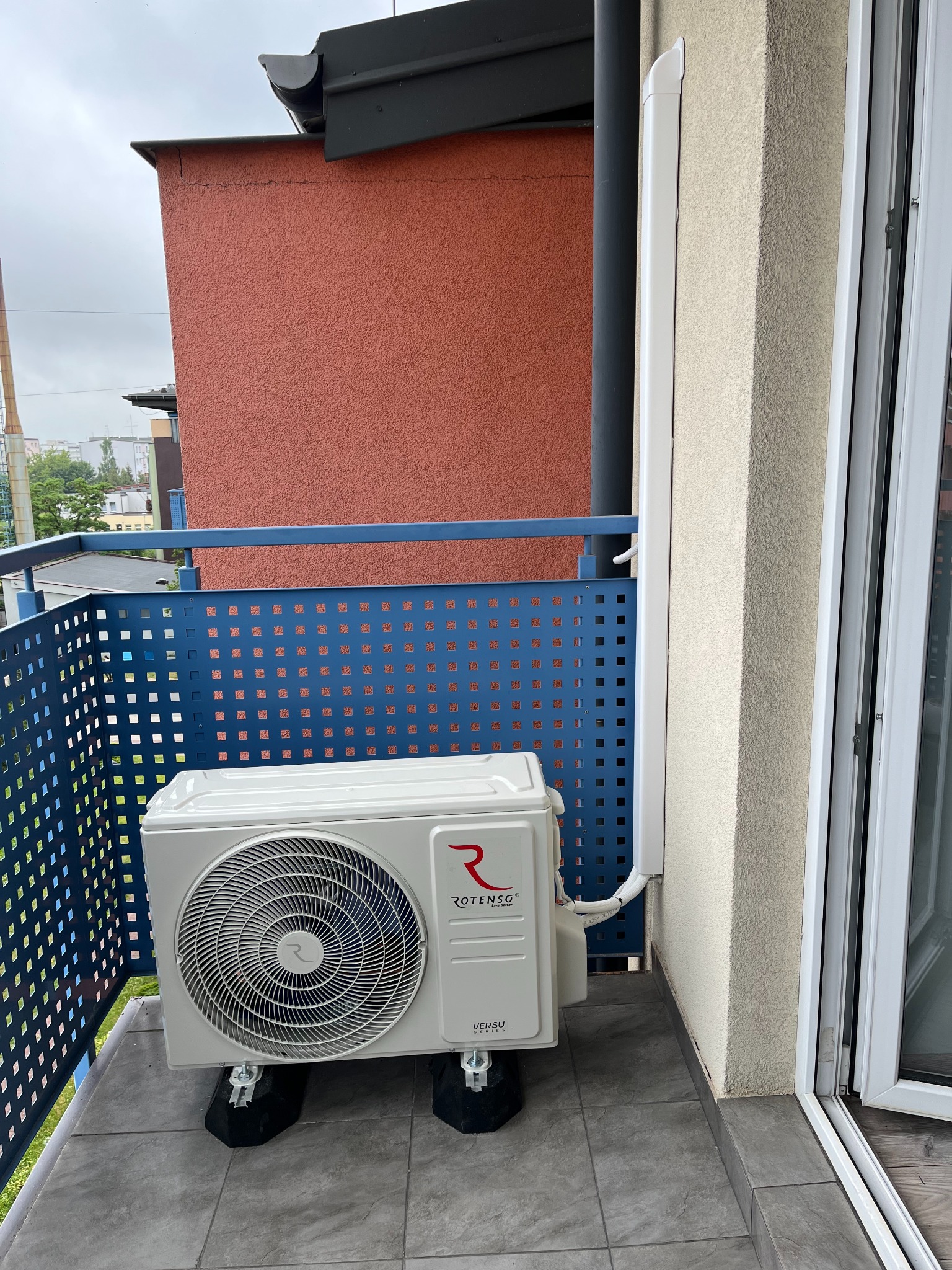 Klimatyzator Rotenso Versu na balkonie w Woli Wiewieckiej, zamontowany na specjalnych podkładkach antywibracyjnych. Widoczne rury odprowadzające skropliny.