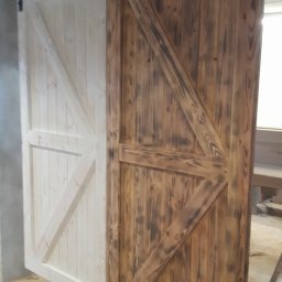 Mik-Mont - Dwie przesuwne drzwi w stylu rustykalnym z drewna, jedna biała, druga opalana, zawieszone na czarnym metalowym systemie przesuwnym.