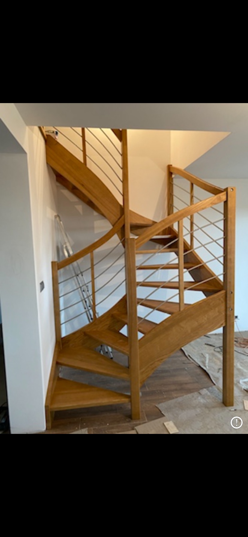 Kręcone schody drewniane z metalowymi poręczami w trakcie montażu, zabezpieczona podłoga, widoczne elementy montażowe.