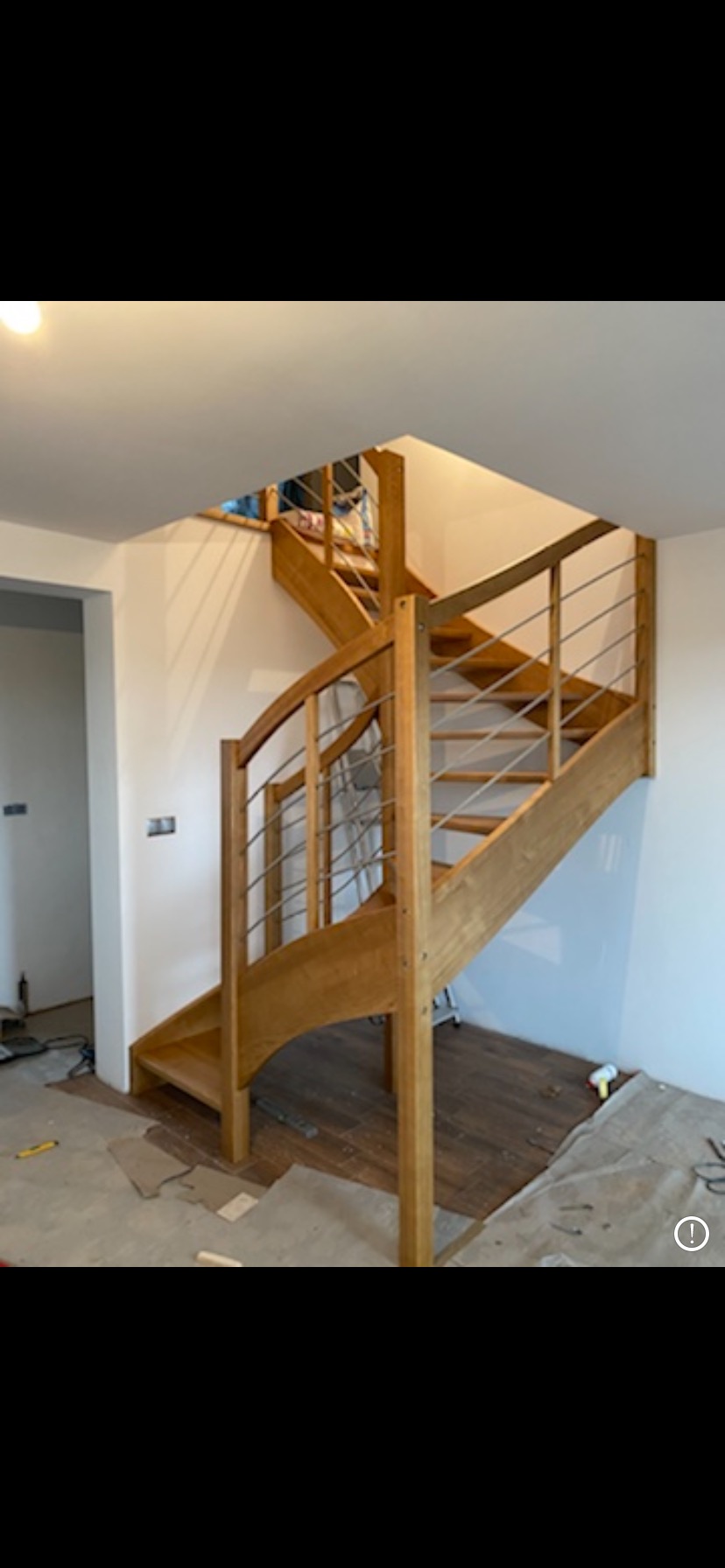 Wnętrze domu w trakcie remontu, ukazujące drewniane schody z metalowymi poręczami, prowadzące na wyższą kondygnację, z widocznymi narzędziami i materiałami zabezpieczającymi podłogę.
