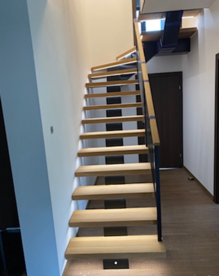 Nowoczesne schody z drewnianymi stopniami i czarnymi wspornikami, oświetlenie LED w dolnej części, minimalistyczny design.