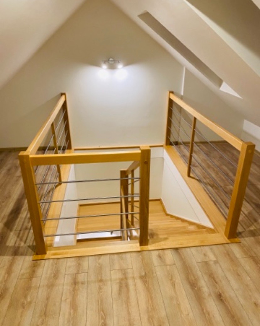 Jasne drewniane schody z poręczami ze stali nierdzewnej, prowadzące na poddasze z oknem dachowym, widok z góry.