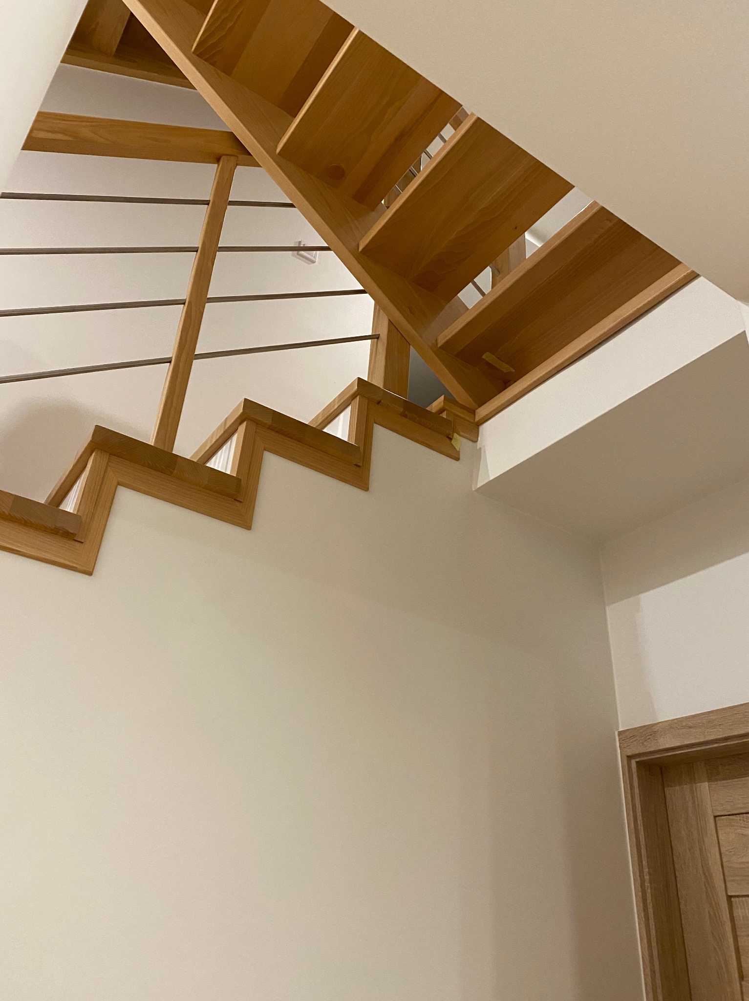 Drewniane schody z metalowymi prętami jako balustradą, widok od dołu, z fragmentem drzwi po prawej stronie.