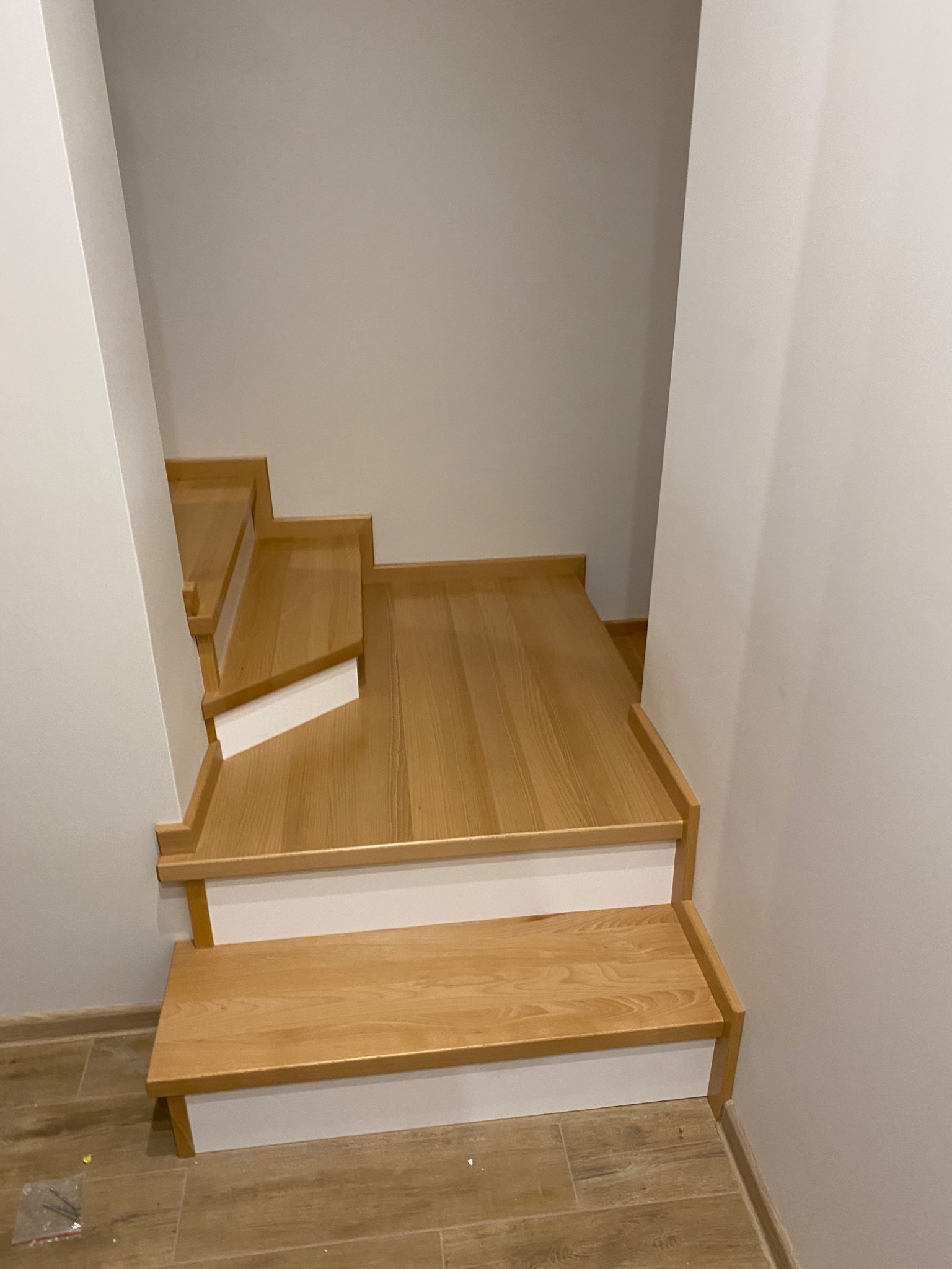 Jasne, drewniane schody z białymi podstopnicami w nowoczesnym wnętrzu, widok z góry na kilka stopni.
