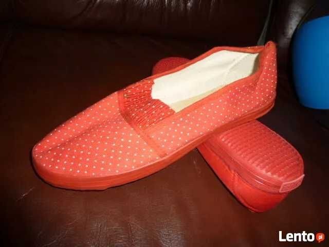 Czerwone damskie baleriny w białe kropki, leżące na ciemnobrązowej skórzanej powierzchni obok niebieskiego wazonu.