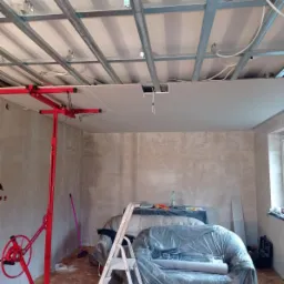 Montaż sufitu podwieszanego z płyt karton gips w Elblągu, widoczny czerwony podnośnik do płyt i metalowa konstrukcja nośna.