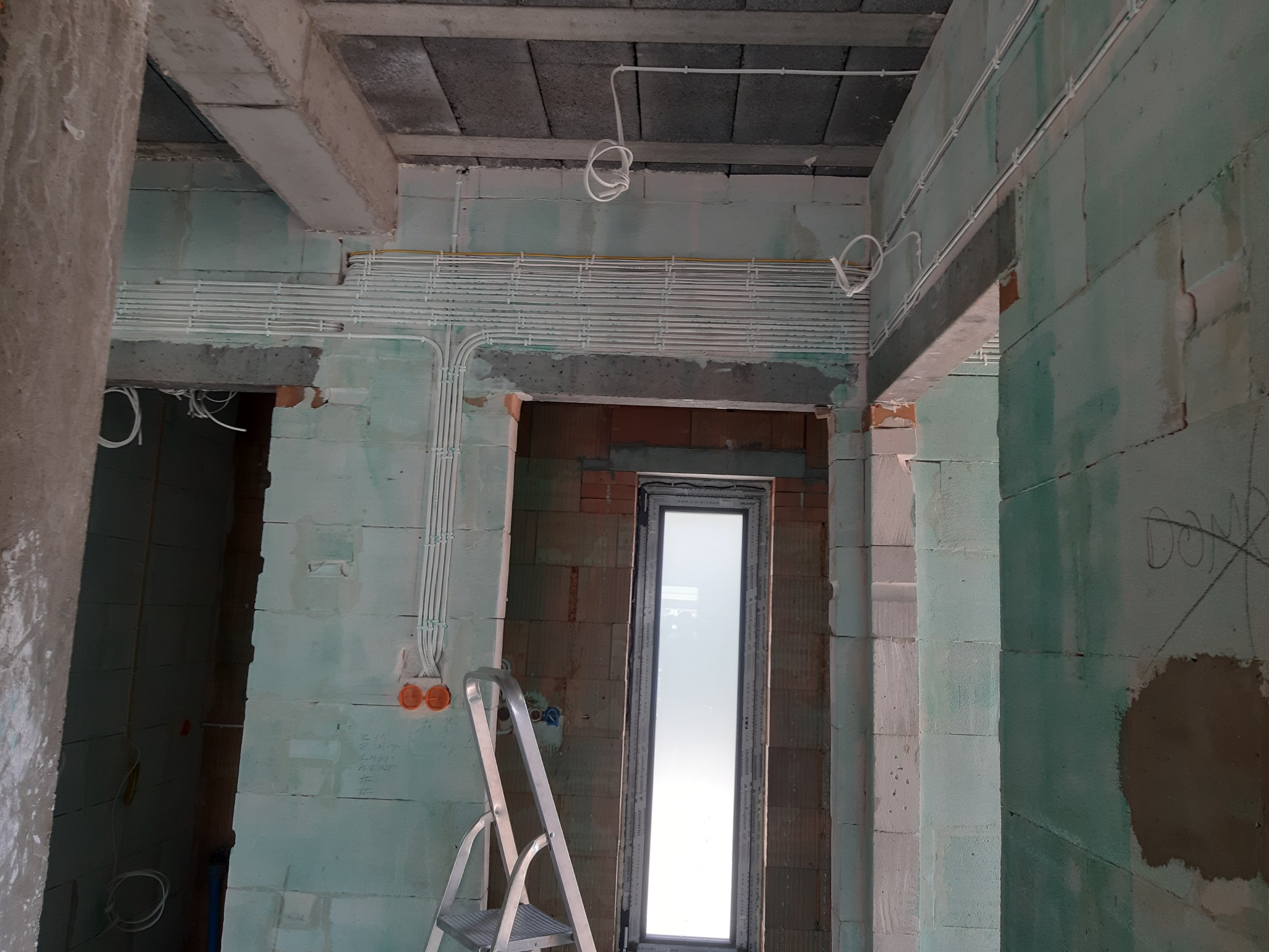 Wnętrze w trakcie prac wykończeniowych w Żninie, widoczne okablowanie elektryczne prowadzone po ścianach i suficie, surowy stan ścian, drabina aluminiowa oparta o ścianę.