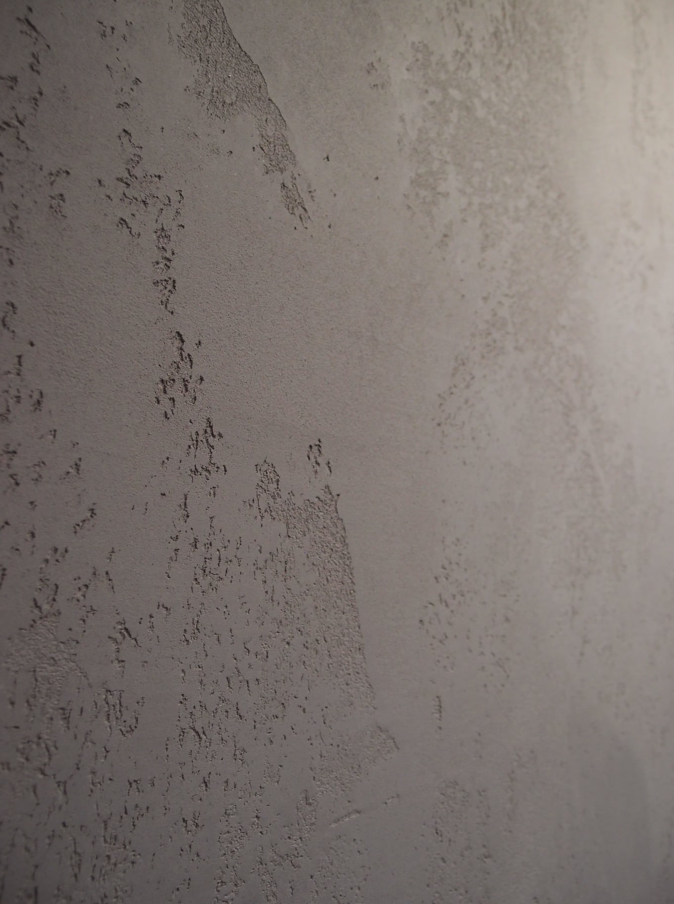 Szara ściana z wyraźną fakturą betonu architektonicznego OIKOS, z widocznymi nieregularnymi wzorami i delikatnymi nierównościami.