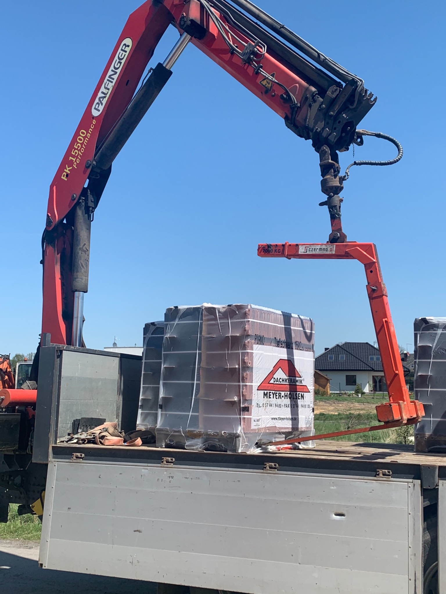 Rozładunek dachówek ceramicznych Meyer-Holsen z użyciem dźwigu Palfinger PK 15500 Performance na skrzynię samochodu ciężarowego.
