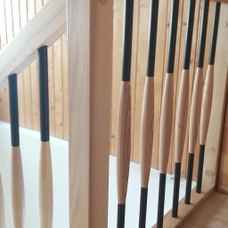 Z.P.U Marek Talaśka - Jasne drewno i czarne elementy nowoczesnej balustrady schodowej z ozdobnymi wrzecionami, widok z dołu, drewniana boazeria w tle.