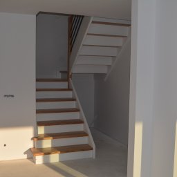 Z.P.U Marek Talaśka - Jasne, nowoczesne schody z drewnianymi stopniami i białymi podstopnicami w surowym wnętrzu. Widoczne niedokończone ściany i otwarte przejście.