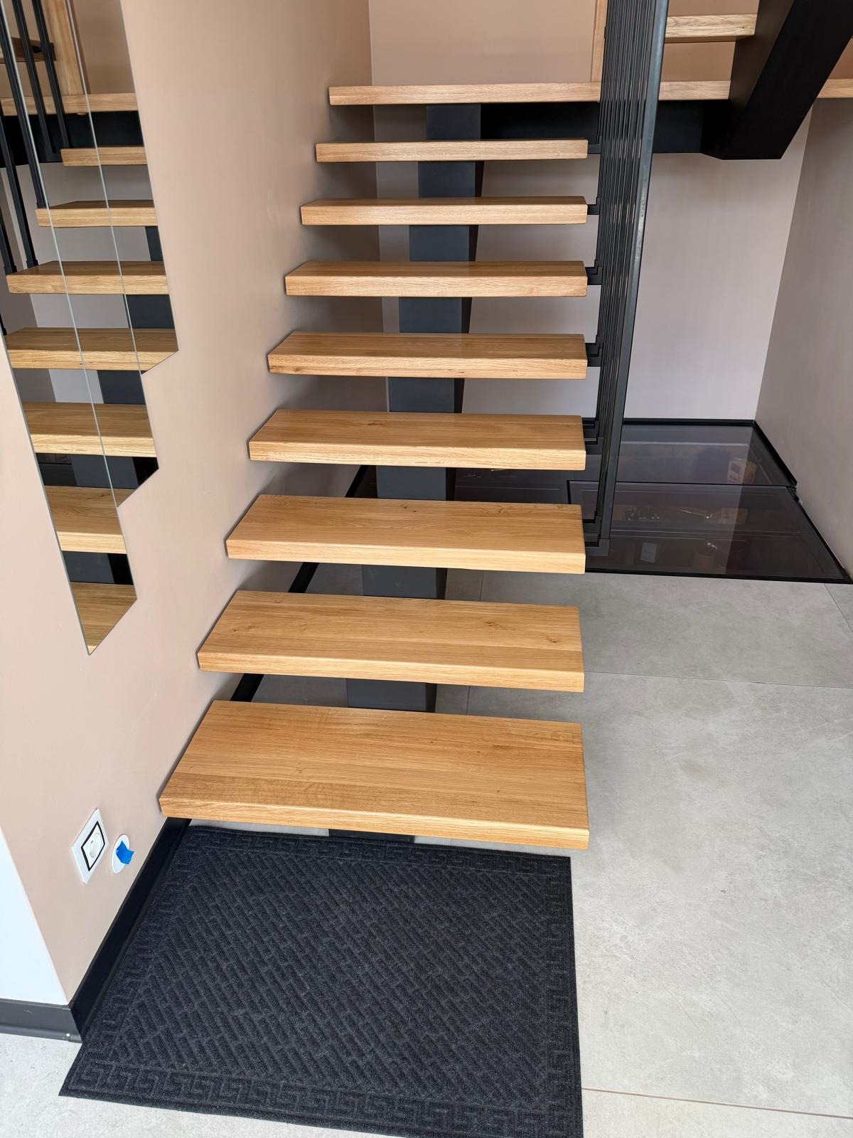 Nowoczesne schody wspornikowe z drewna i metalu w Osie. Widoczne stopnie dębowe i czarna, metalowa konstrukcja. Minimalistyczny design i szklana podłoga w tle.