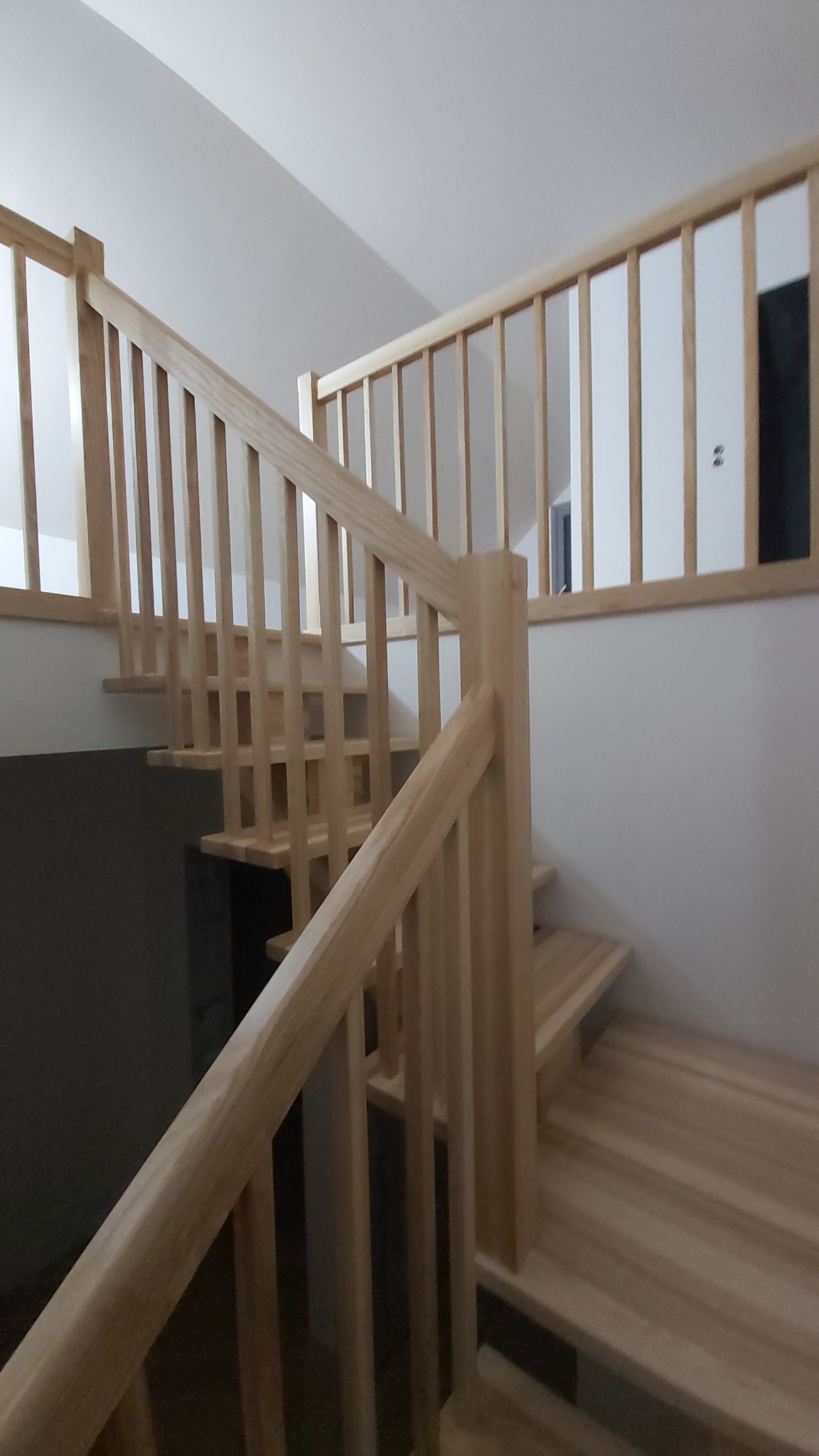 Jasne, drewniane schody z balustradą w domu w Osie. Naturalne wykończenie i prosta konstrukcja. Widok od dołu, podkreślający detale i solidność wykonania.