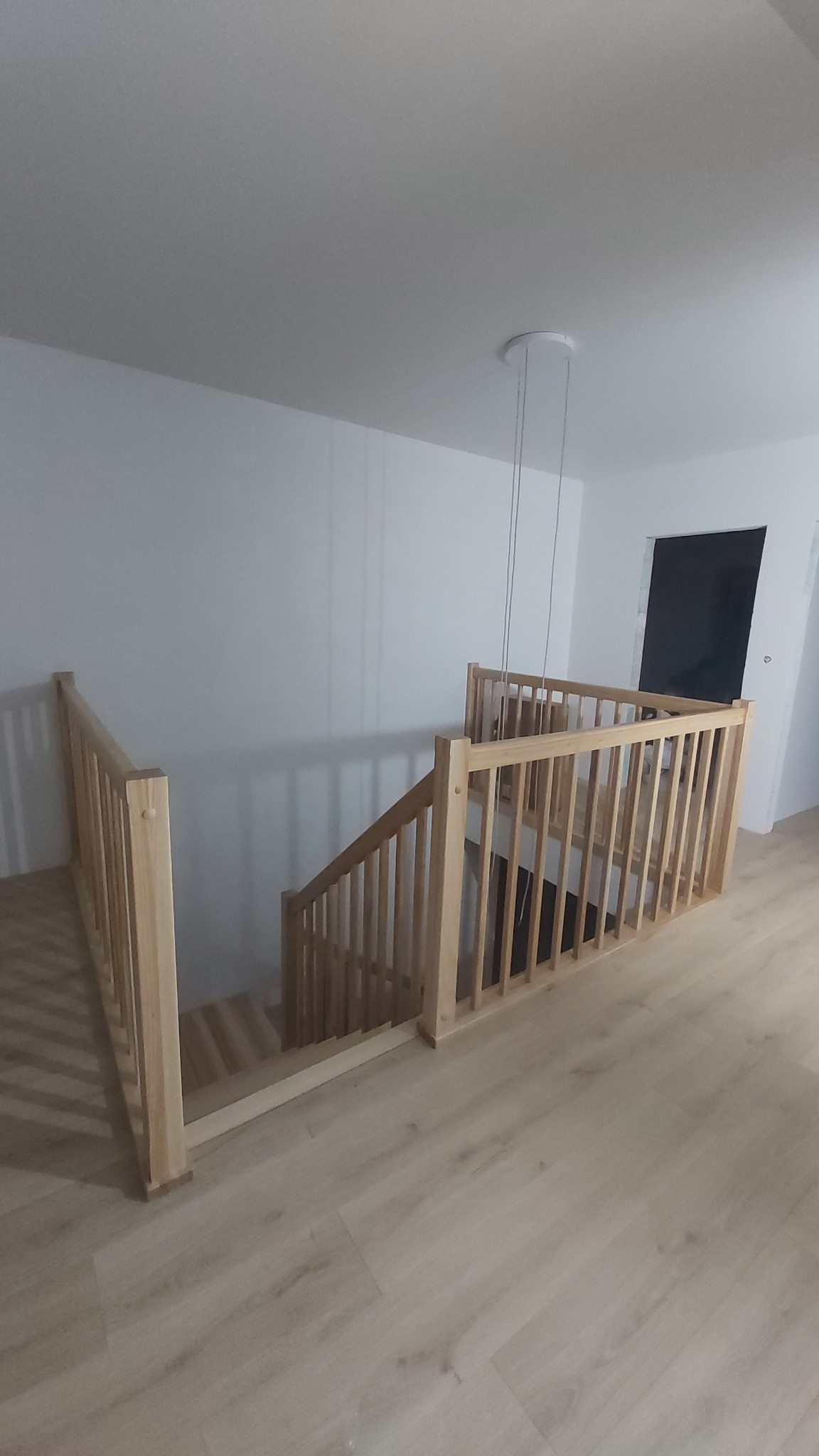 Jasne, drewniane schody z balustradą w nowoczesnym wnętrzu. Widok z góry na schody i fragment podłogi. Minimalistyczny design, naturalne światło.