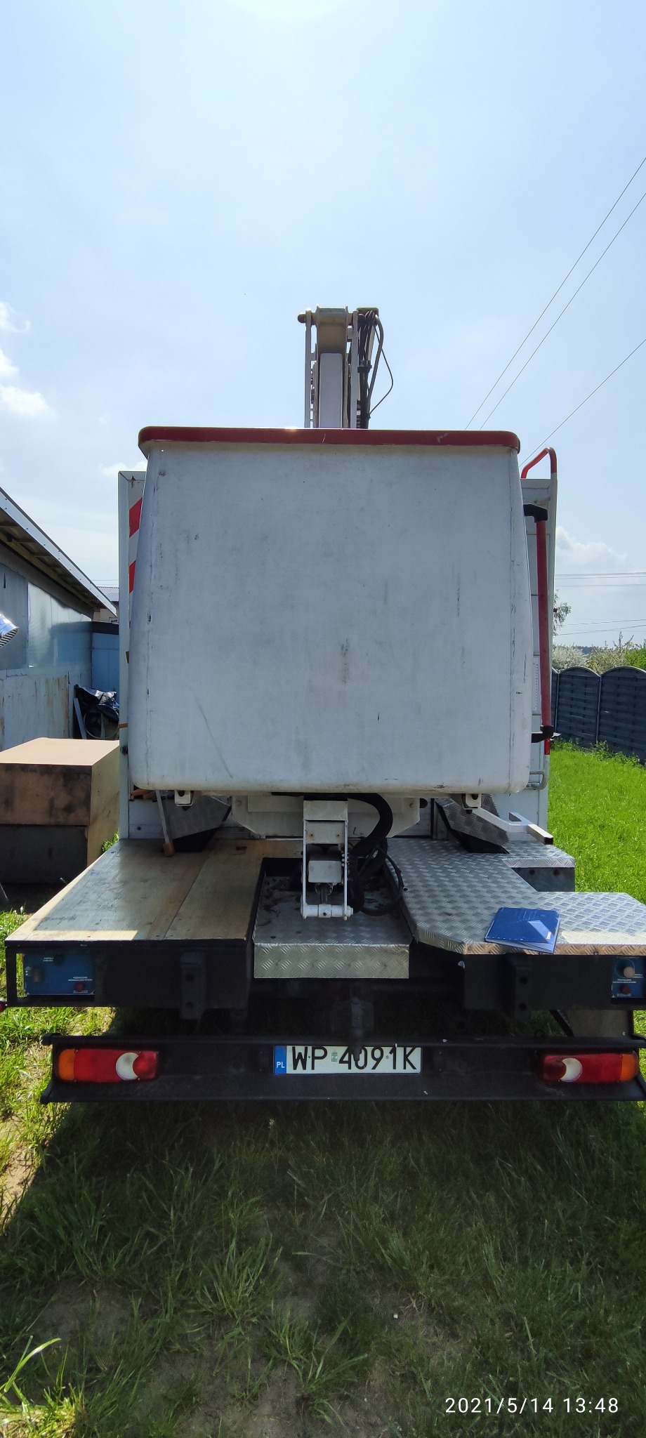 Widok z tyłu na podnośnik koszowy zamontowany na platformie samochodu, z widoczną tablicą rejestracyjną WP 4091K i niebieskim notatnikiem leżącym na platformie.