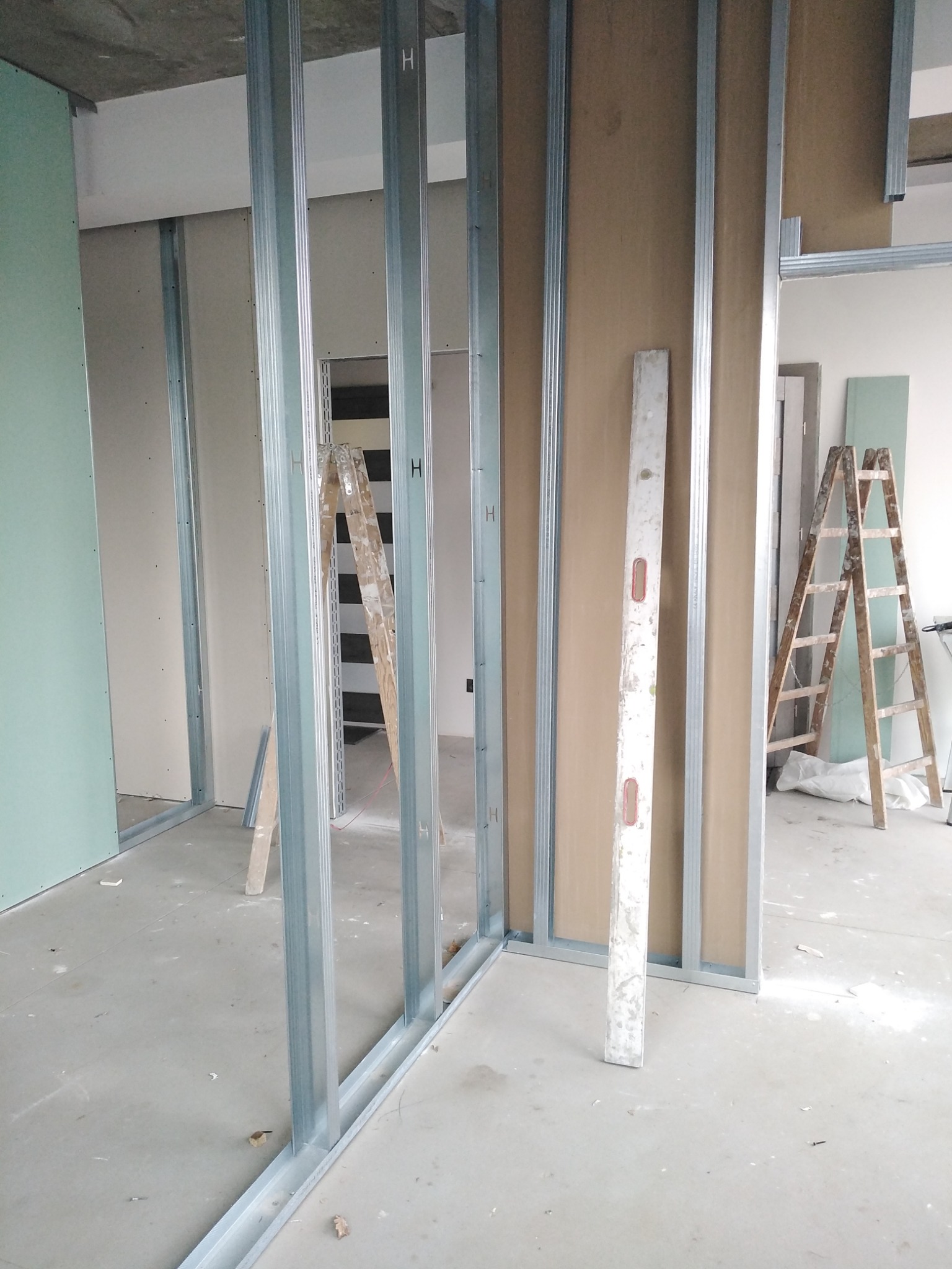 Montaż ścian działowych z płyt gipsowo-kartonowych na metalowym stelażu, widoczna poziomica i drabina, surowy stan wykończenia.