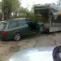 Zielone kombi Audi z otwartymi drzwiami wjeżdża po rampie na platformę transportową przykrytą szarą plandeką, widoczny numer rejestracyjny z Wielkiej Brytanii.
