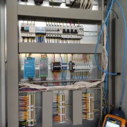 Rozdzielnica elektryczna z widocznymi elementami sterującymi, przewodami i testerem kabli DSX-600, wskazującym na pomiary instalacji.