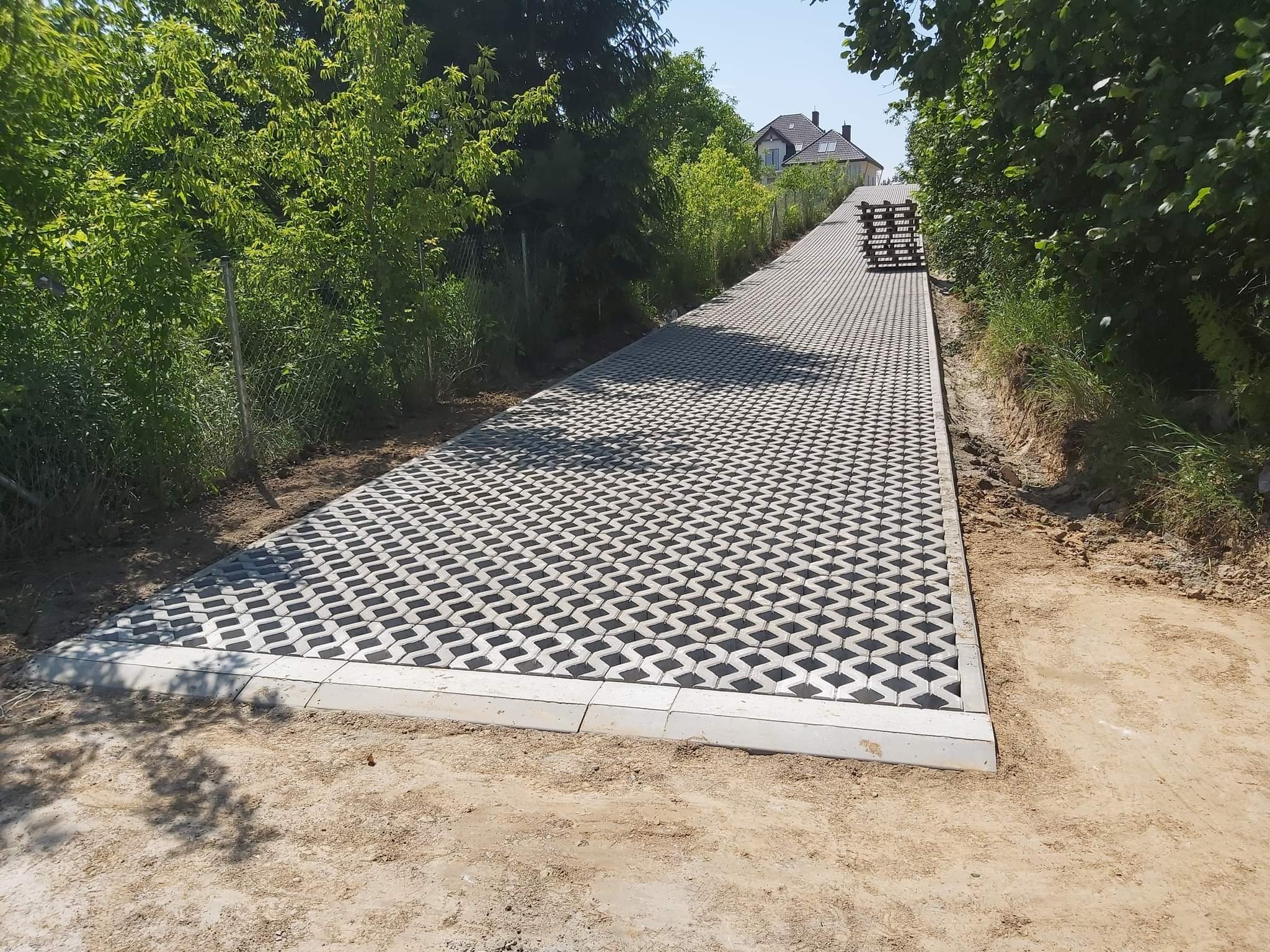 Ułożona ażurowa kostka brukowa na podjeździe, obrzeża z jasnego betonu, w tle zieleń i dom.