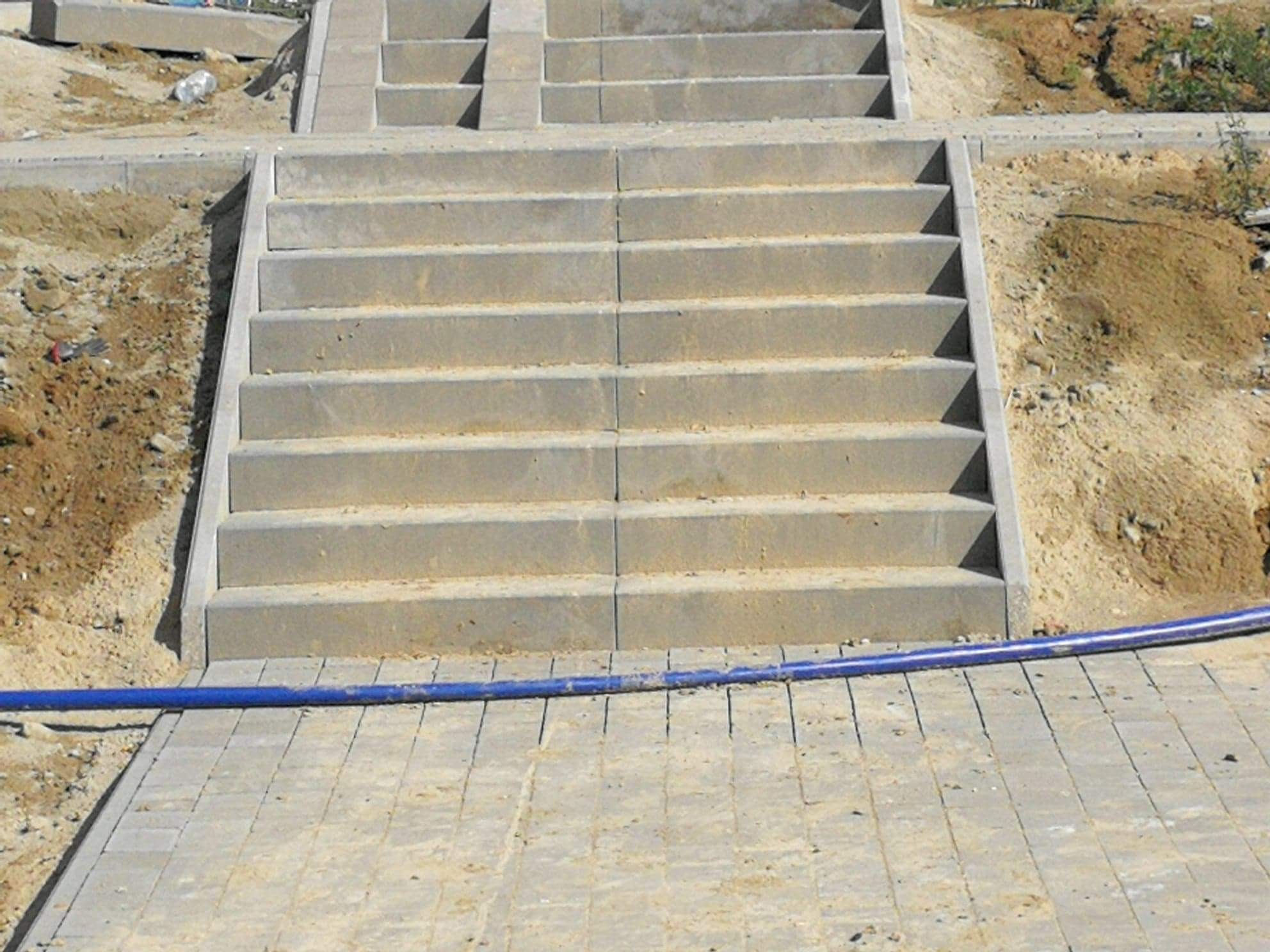 Betonowe schody prowadzące w górę, otoczone ziemią i kostką brukową, z niebieskim wężem leżącym na kostce.