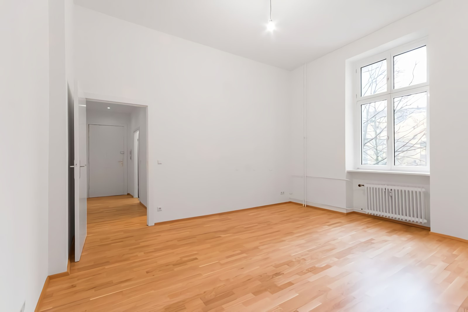 Jasny pokój z parkietem po renowacji, widoczna faktura drewna i brak śladów użytkowania, białe ściany, okno z widokiem na drzewa.